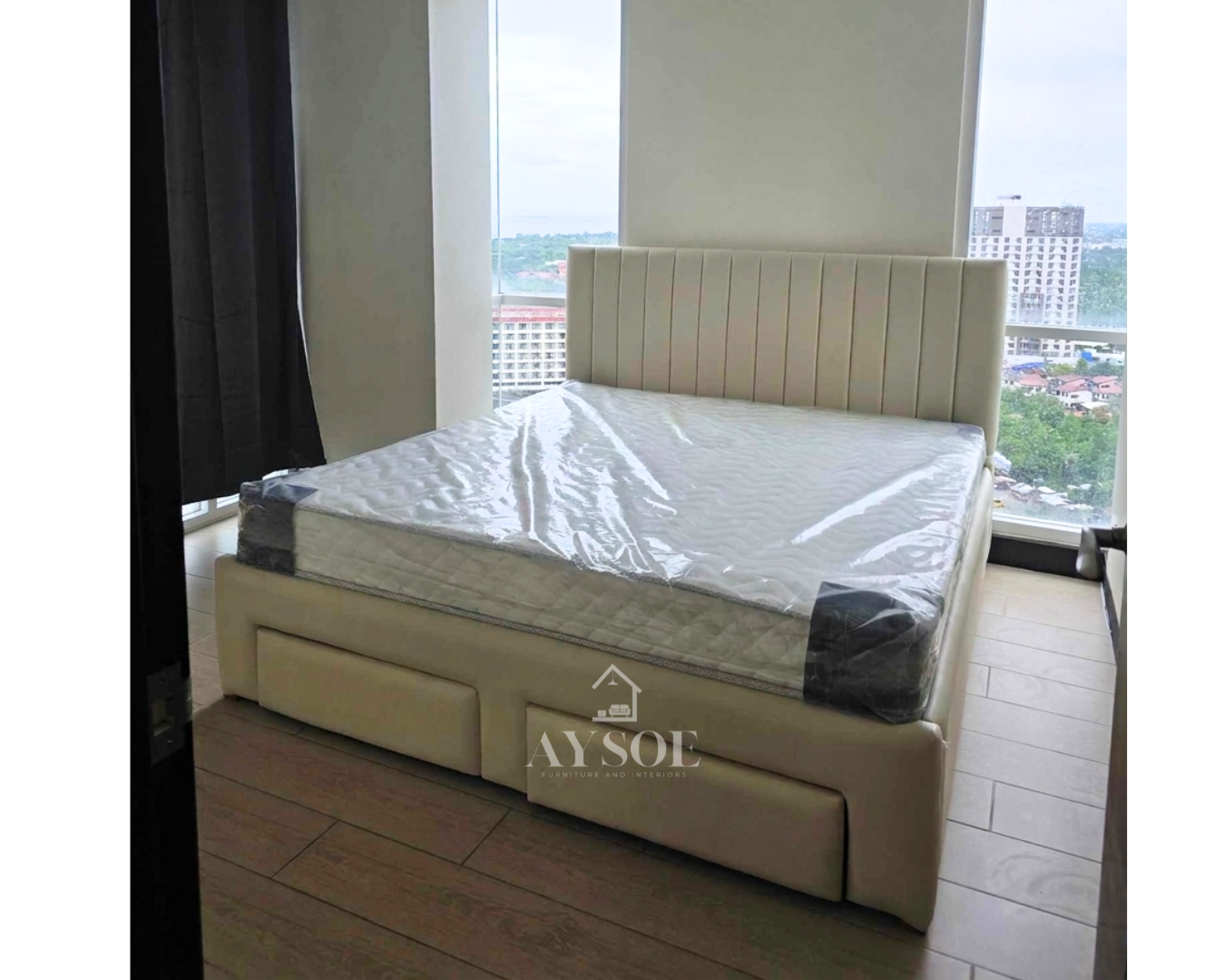 An upholstered bed frame in soft cream leatherette, with a channel-tufted headboard and two roomy pull-out drawers. Clean, modern, and space-saving.