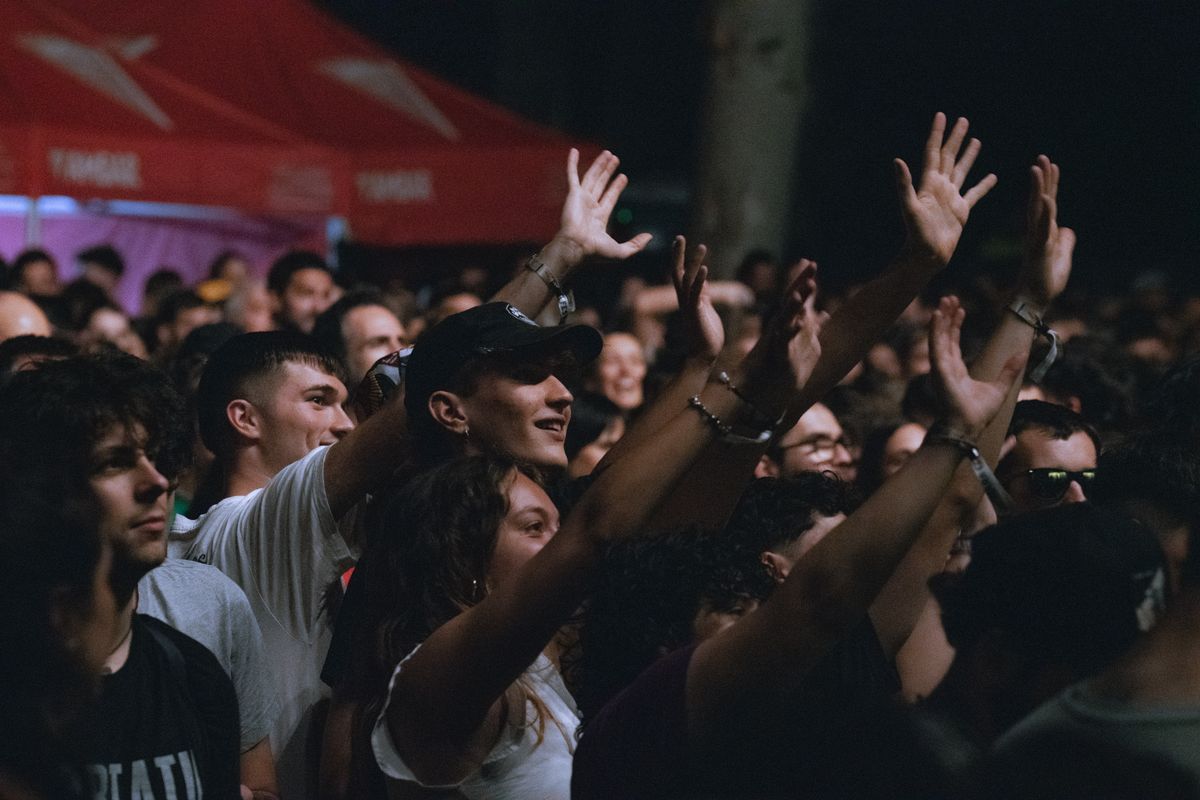 An energetic crowd facing an outdoor music festival stage at night