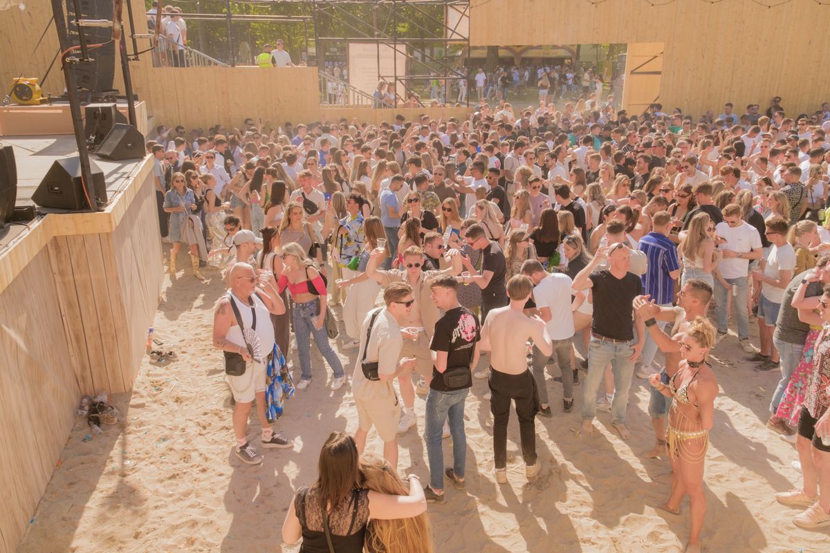 A large crowd enjoying a sunny music festival beside the beach