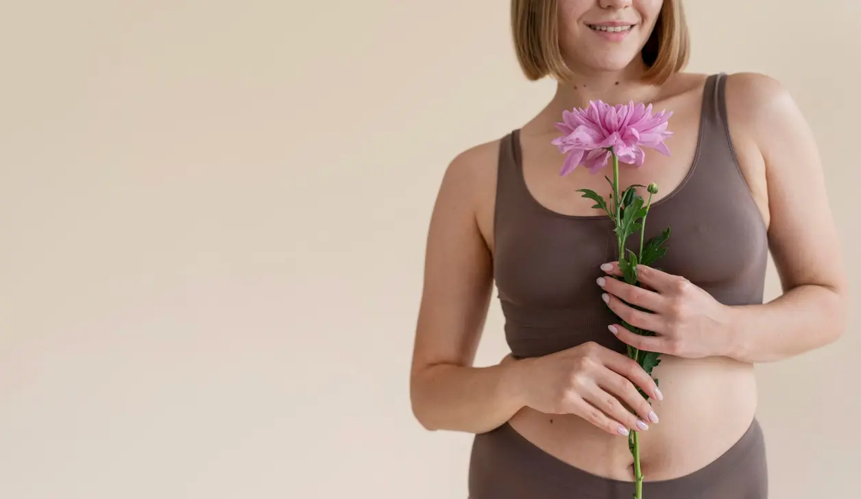 Mujer sonriente en ropa interior sostiene una flor rosa frente al vientre