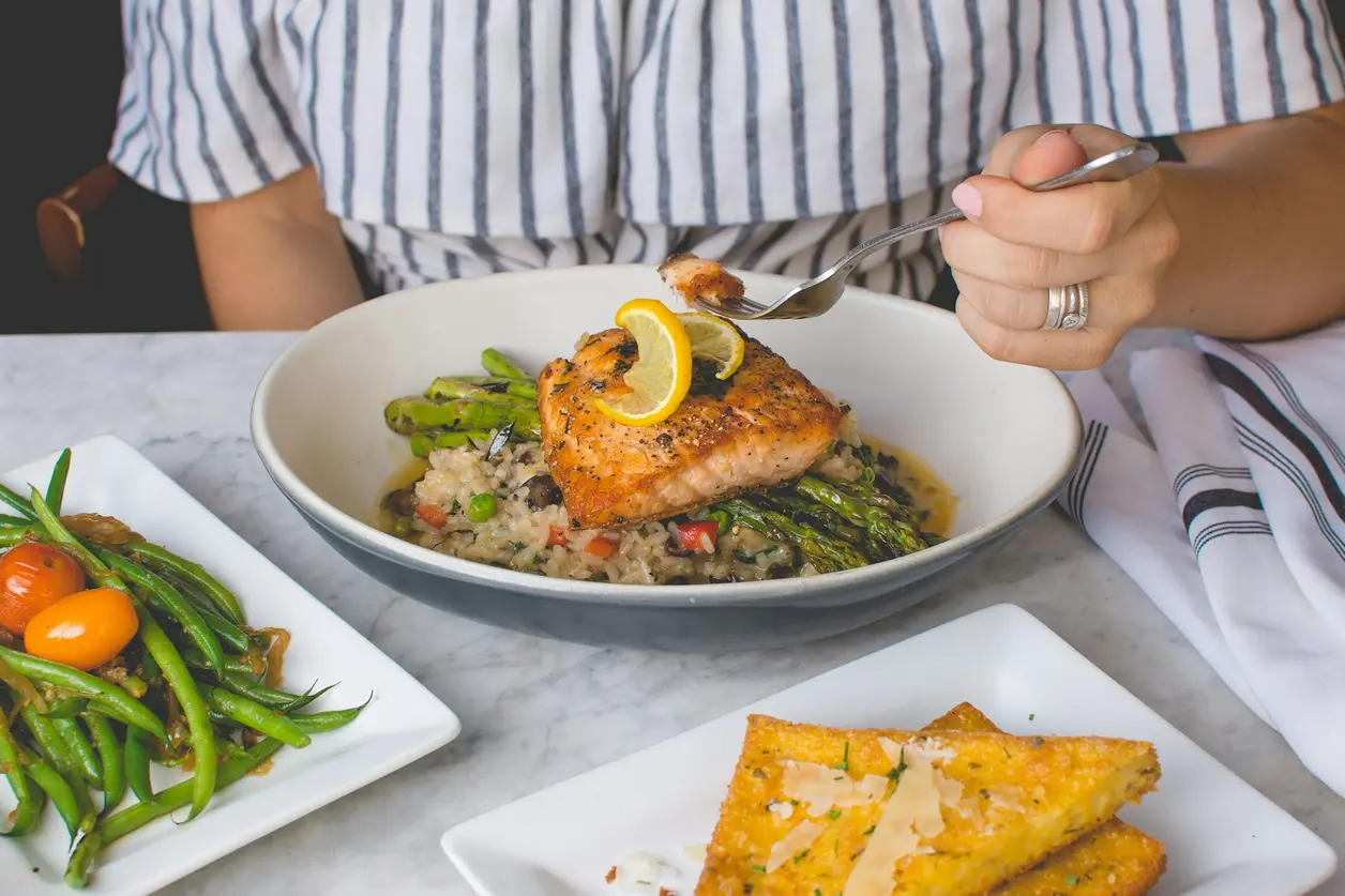 Mujer come salmón a la plancha con quinoa, espárragos y judías verdes