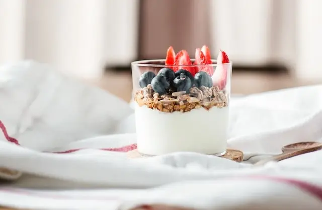 Vaso de yogur con granola, arándanos y fresas sobre la cama