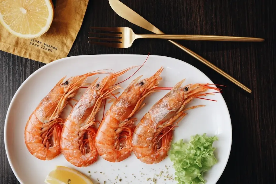 Plato de gambas cocidas con limón y cubiertos dorados
