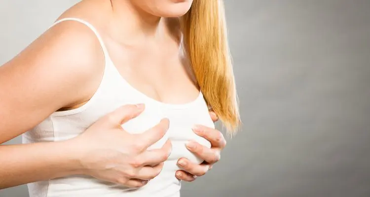 Mujer con camiseta blanca se sujeta el pecho con las manos