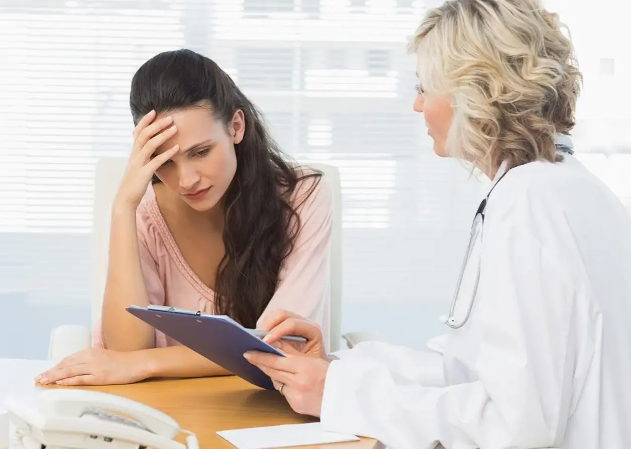 Mujer preocupada escucha a su médica, que sostiene una carpeta