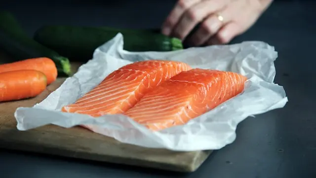 Lomos de salmón crudo sobre papel, junto a zanahorias y calabacines
