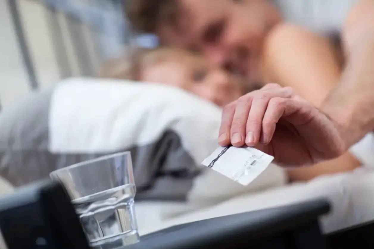 Mujer en la cama coge un blíster de pastillas de la mesita junto a un vaso de agua