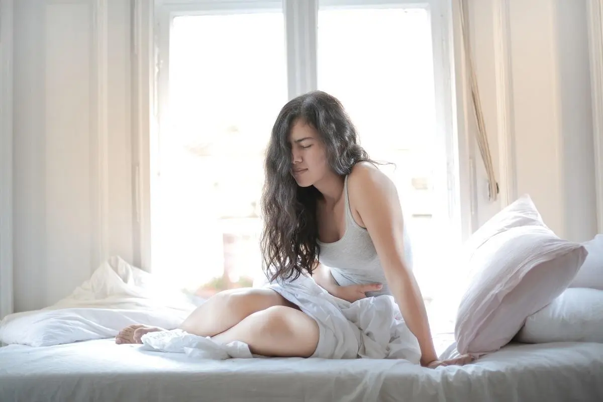 Mujer sentada en la cama junto a la ventana con la mano en el vientre
