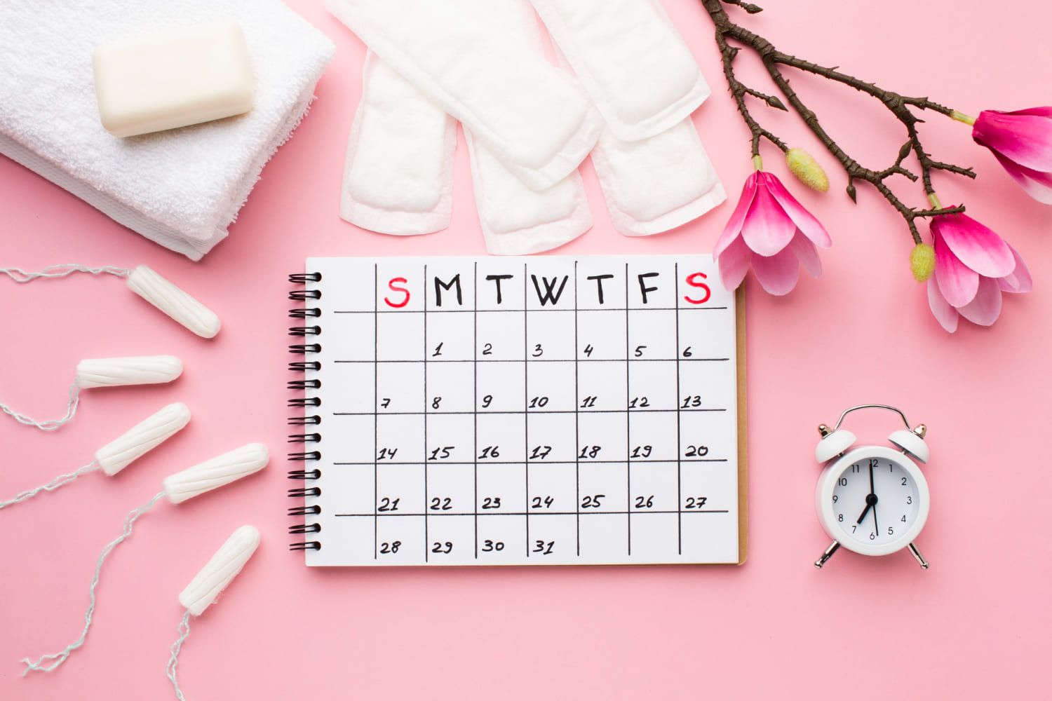 Calendario, compresas, tampones y flores de magnolia sobre fondo rosa