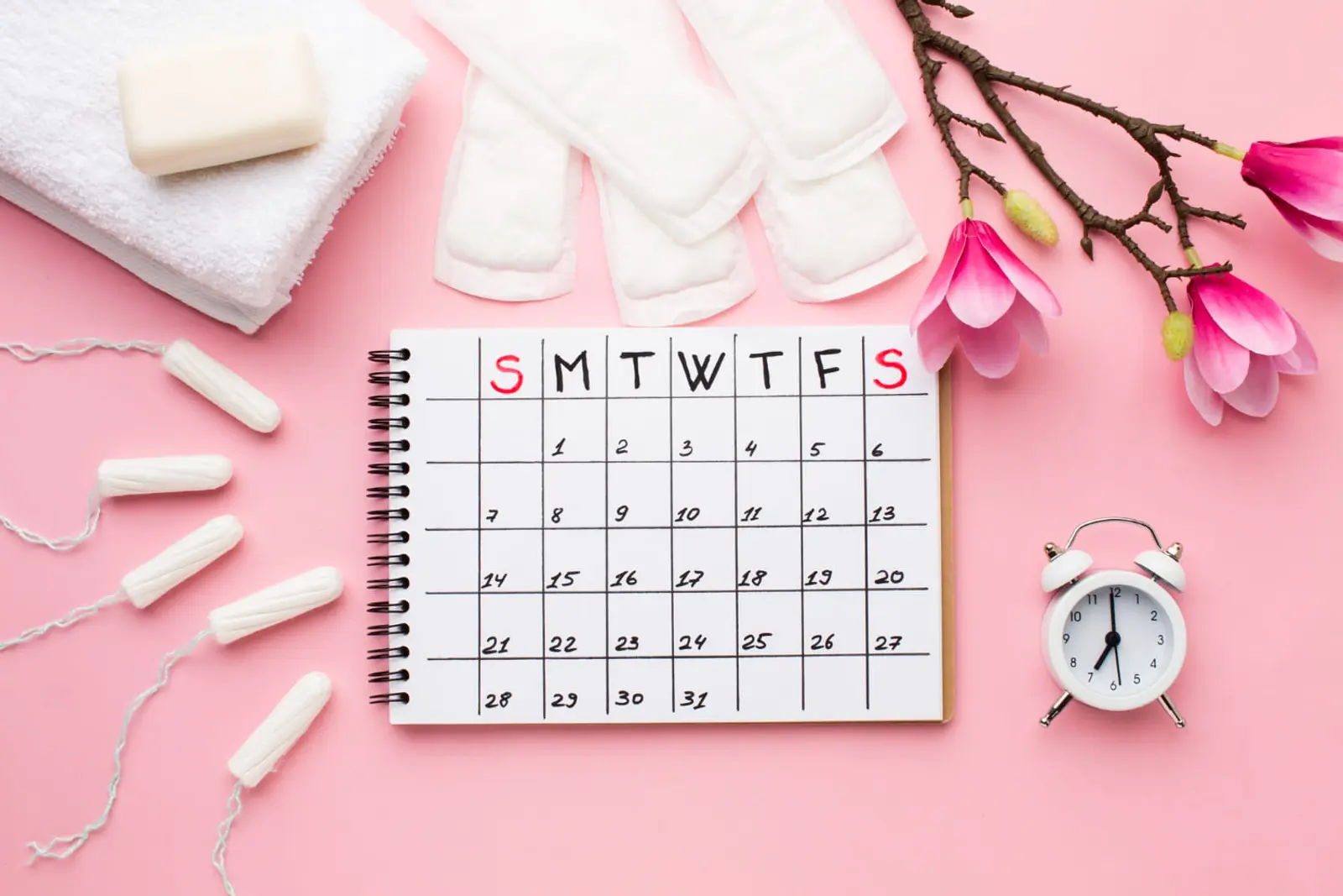 Calendario, compresas, tampones y flores de magnolia sobre fondo rosa