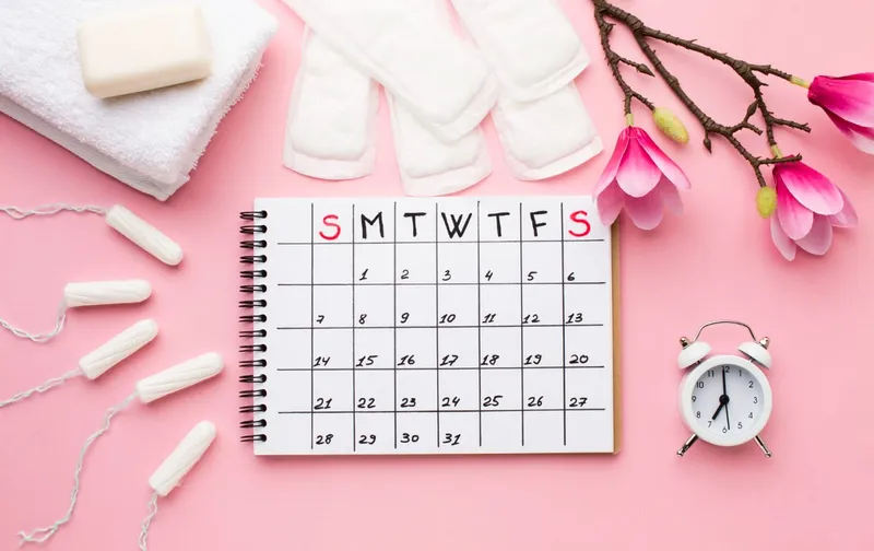 Calendario, compresas, tampones y flores de magnolia sobre fondo rosa