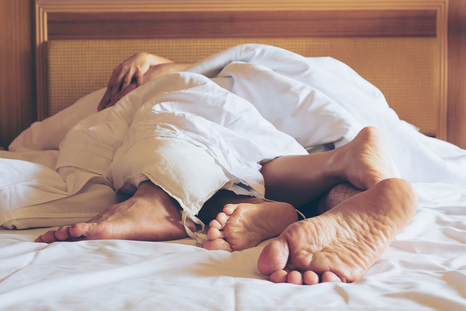 Pareja abrazada bajo las sábanas con los pies asomando