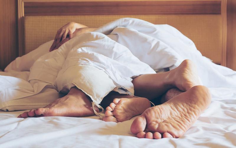 Pareja abrazada bajo las sábanas con los pies asomando