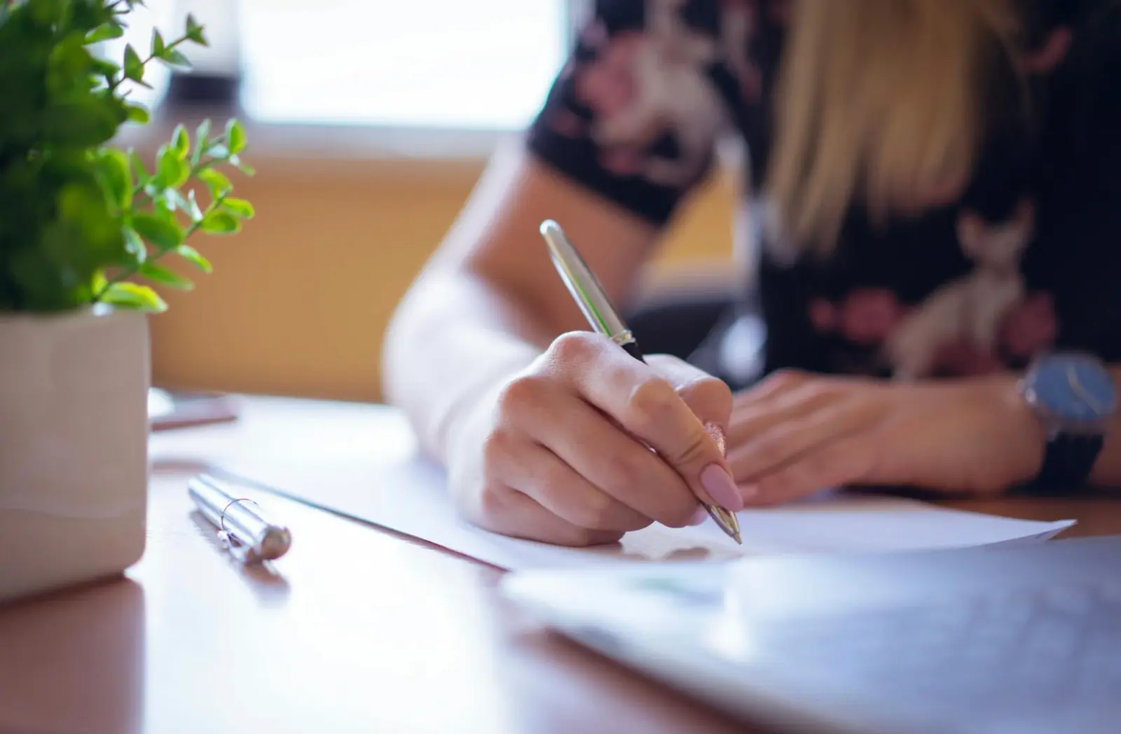 Mujer escribe con bolígrafo en una libreta sobre un escritorio con una planta