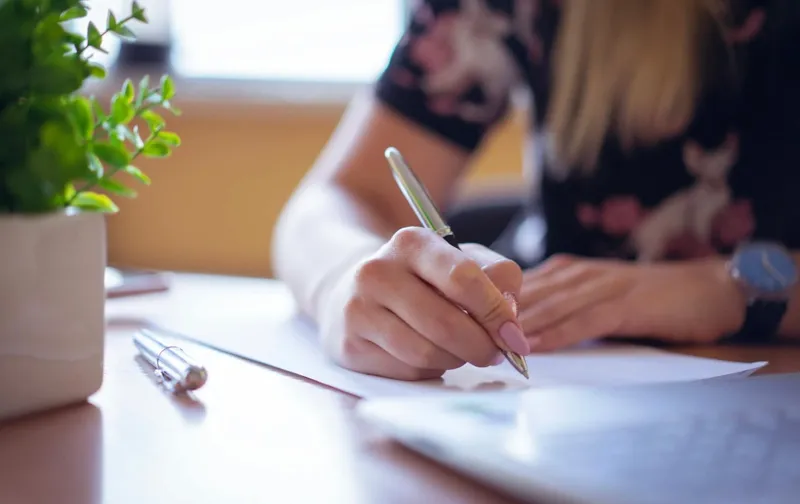 Mujer escribe con bolígrafo en una libreta sobre un escritorio con una planta