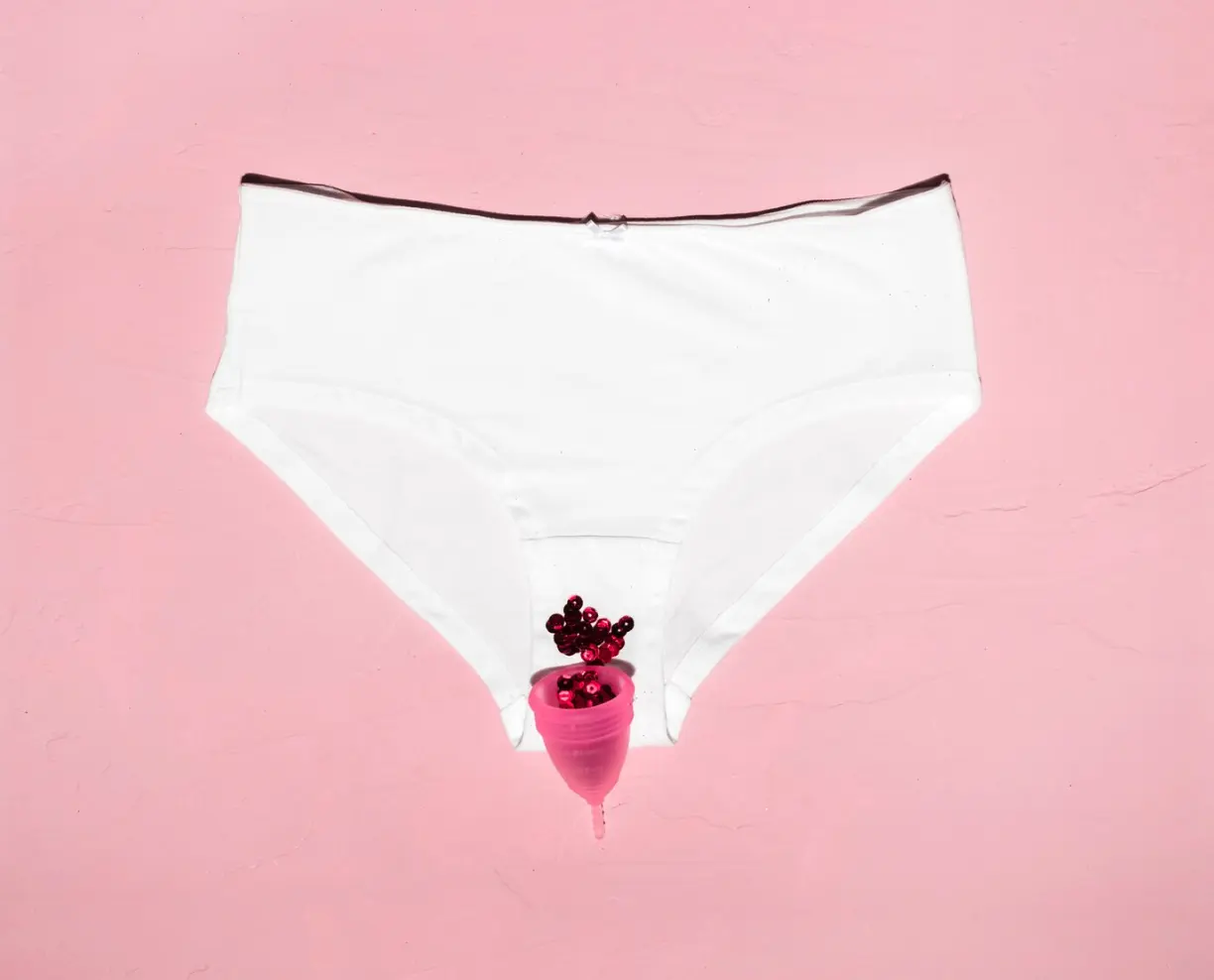 Braguita blanca con copa menstrual rosa y lentejuelas rojas sobre fondo rosa