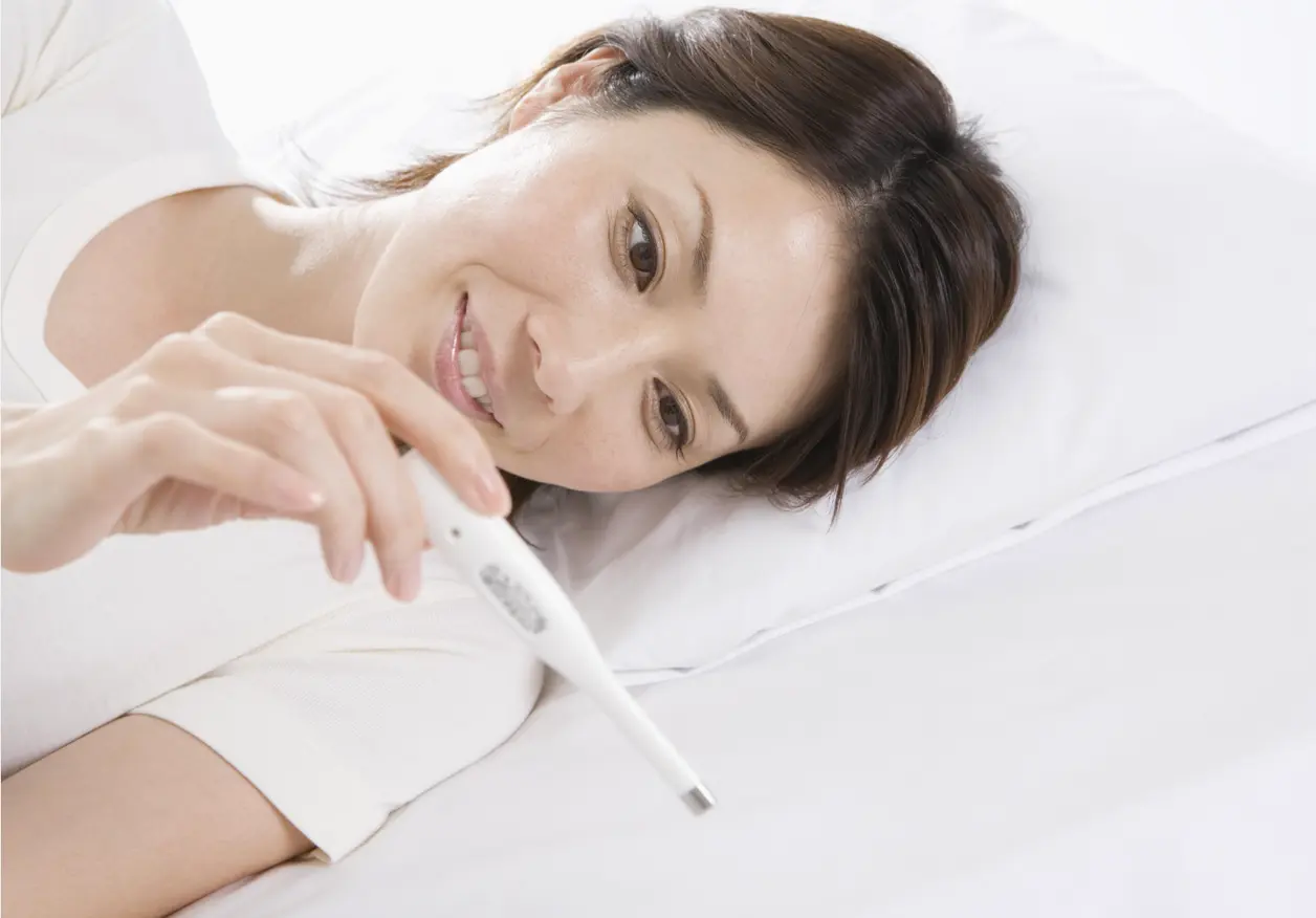 Mujer tumbada en la cama mira sonriente un termómetro