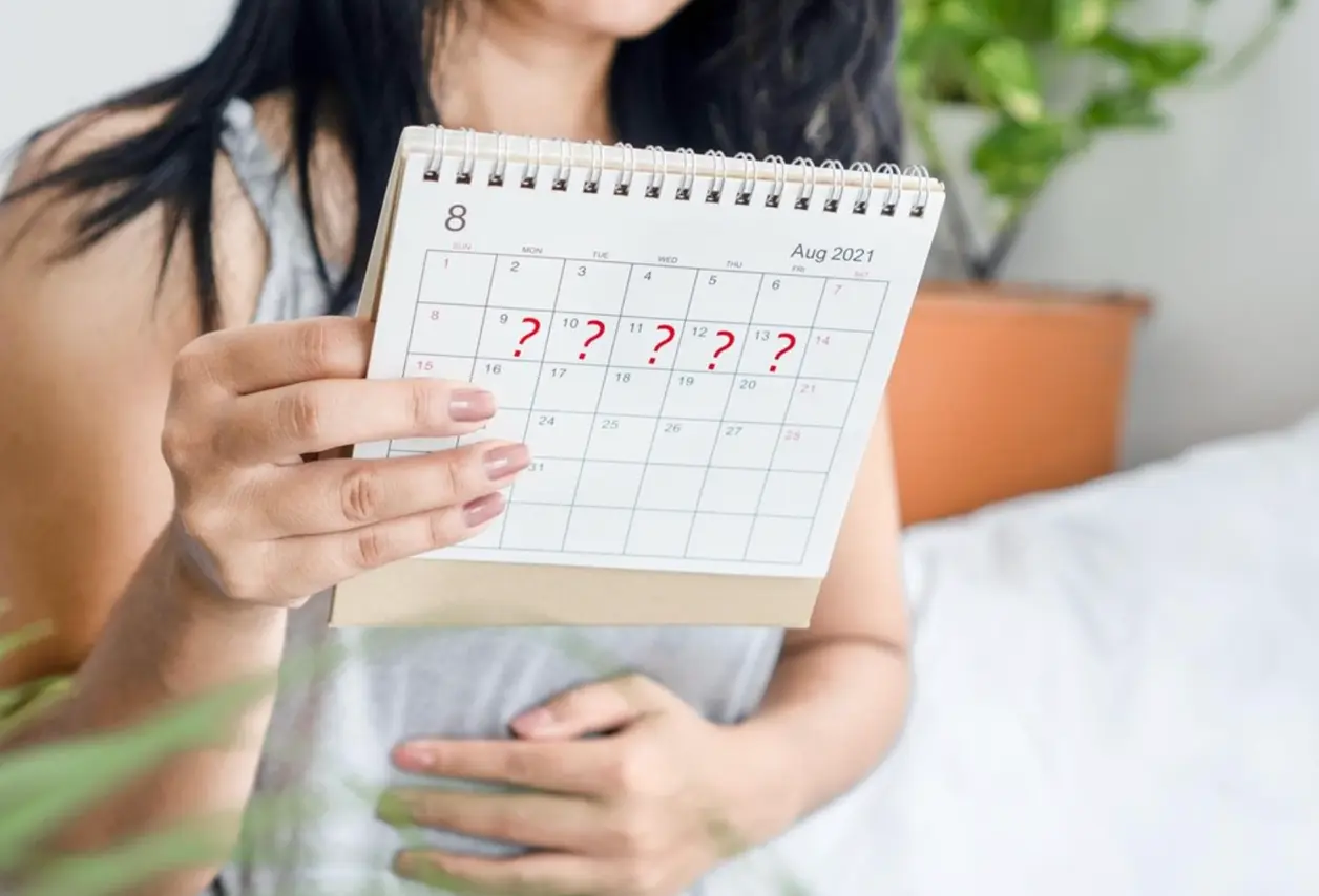Mujer muestra un calendario con varios días marcados con interrogantes rojos