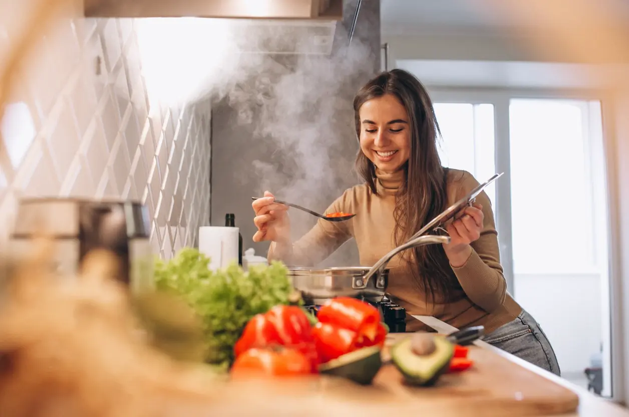 Mujer sonriente cocina en una olla junto a pimientos, aguacate y lechuga