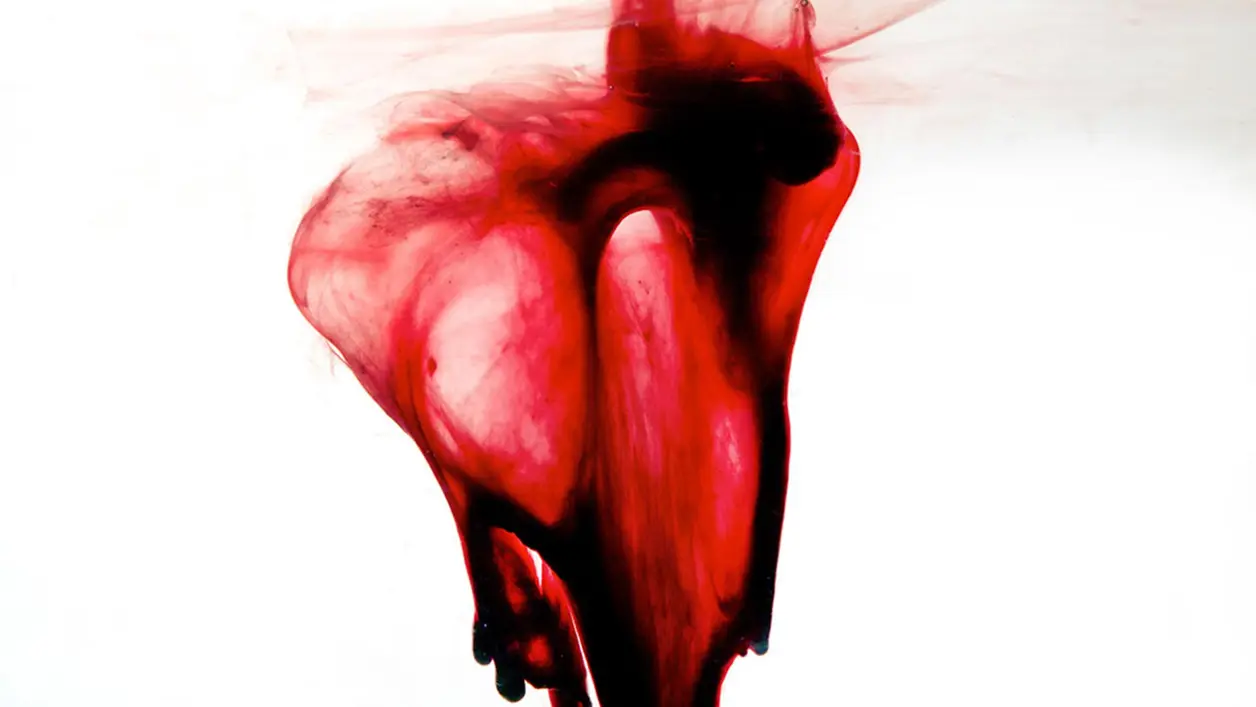 Tinta roja disolviéndose en agua sobre fondo blanco