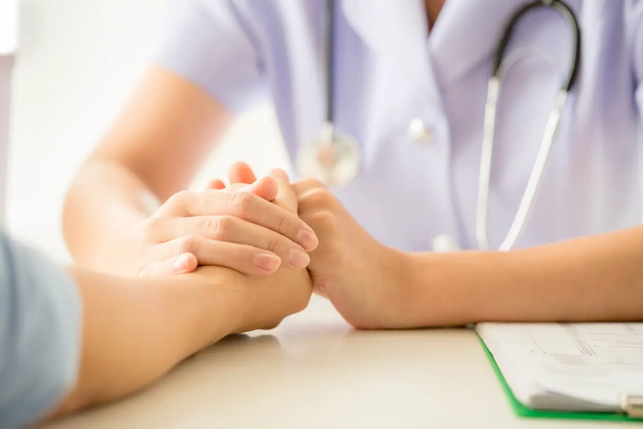 Médica con estetoscopio sujeta las manos de una paciente sobre la mesa