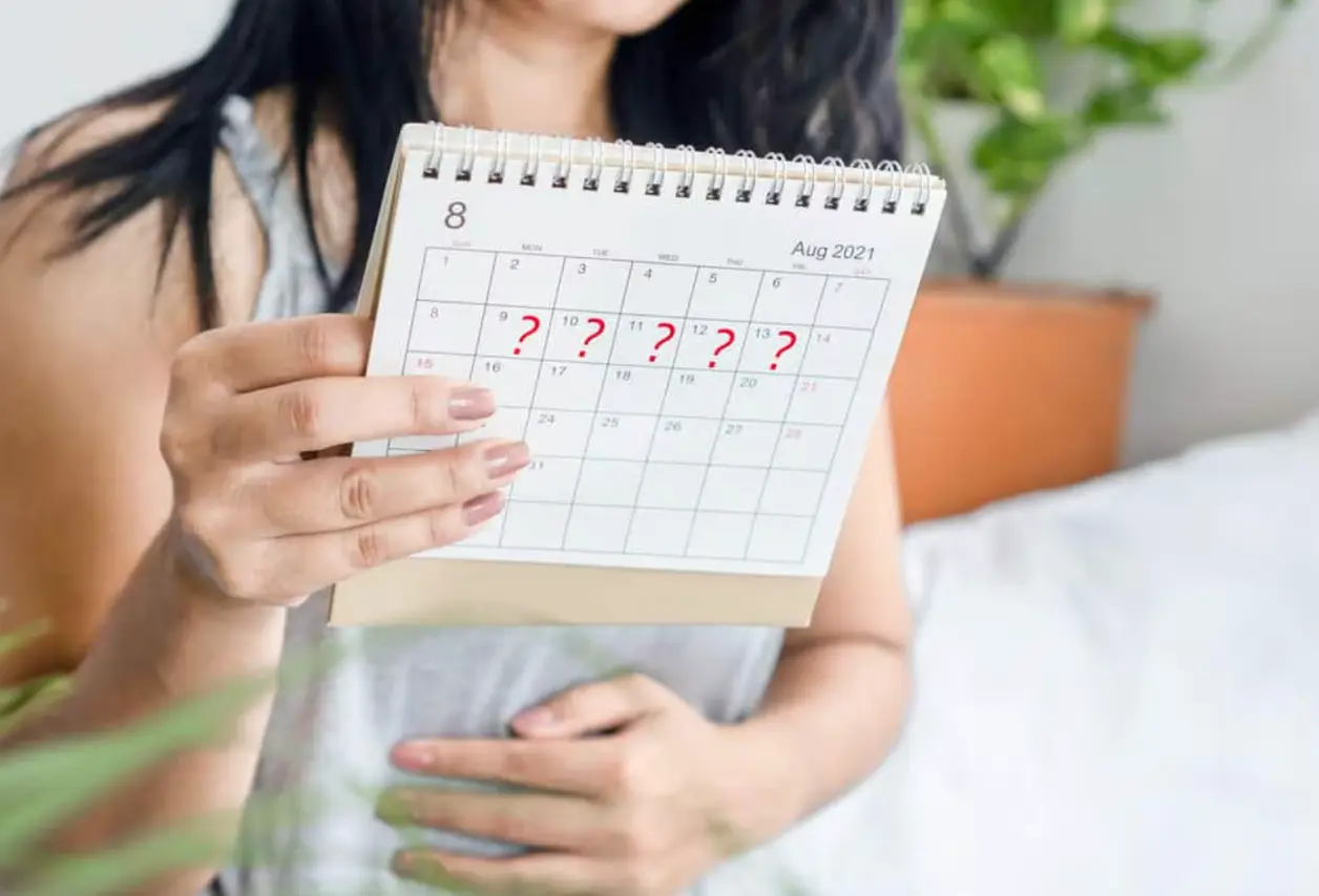 Mujer muestra un calendario con varios días marcados con interrogantes rojos