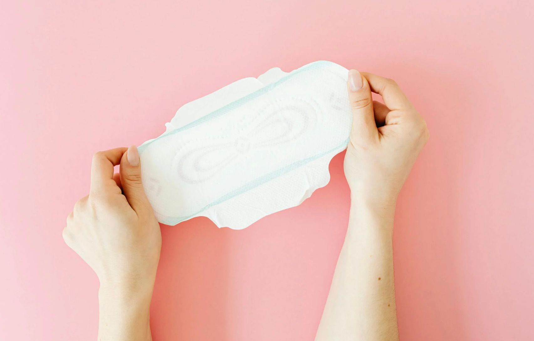 Manos sostienen una compresa sobre un fondo rosa