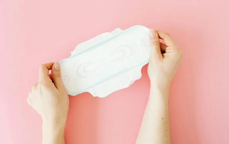 Manos sostienen una compresa sobre un fondo rosa