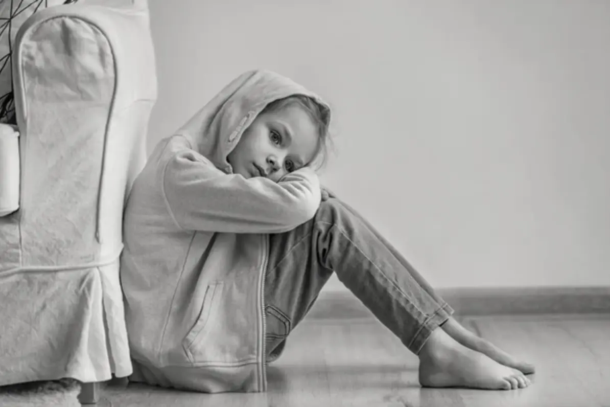 Niña con sudadera con capucha sentada en el suelo, en blanco y negro