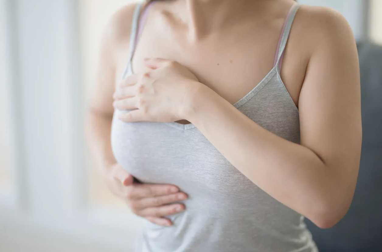 Mujer con top gris se toca el pecho con gesto de dolor