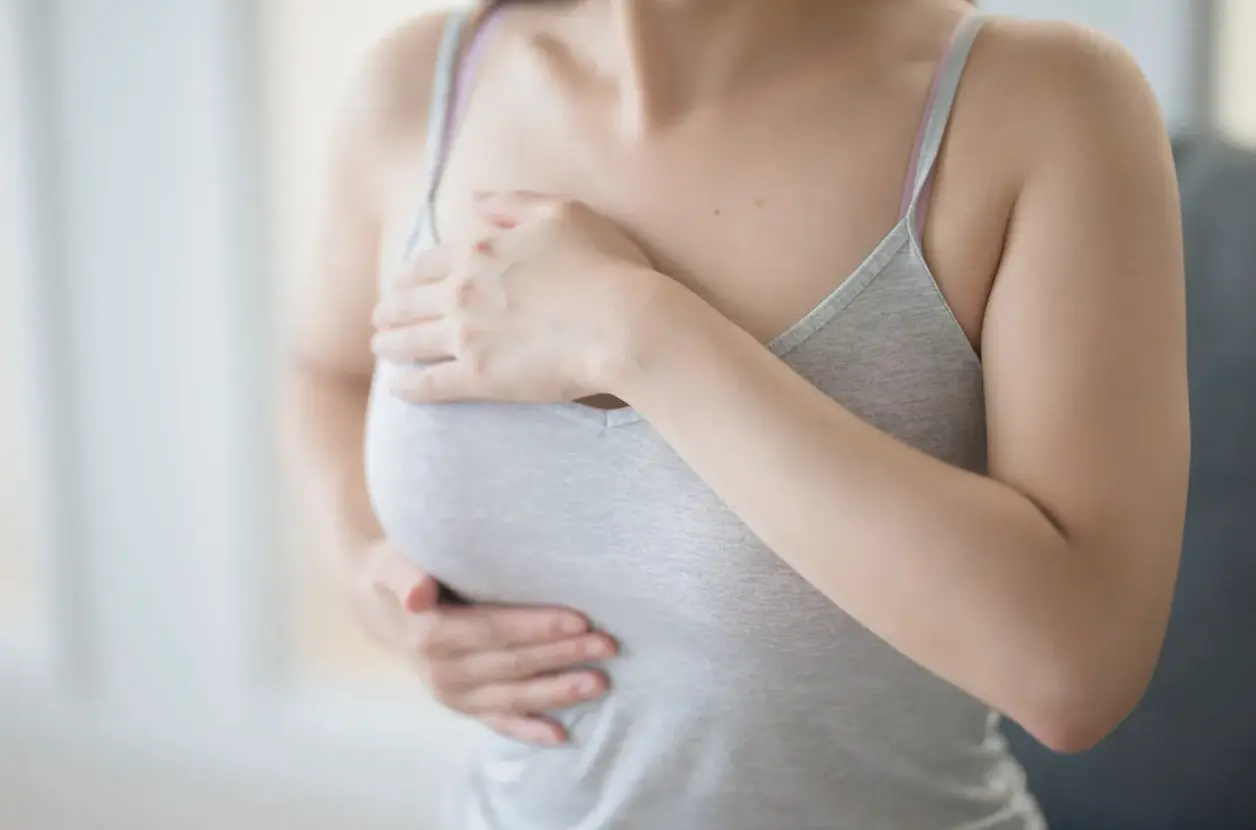 Mujer con top gris se toca el pecho con gesto de dolor