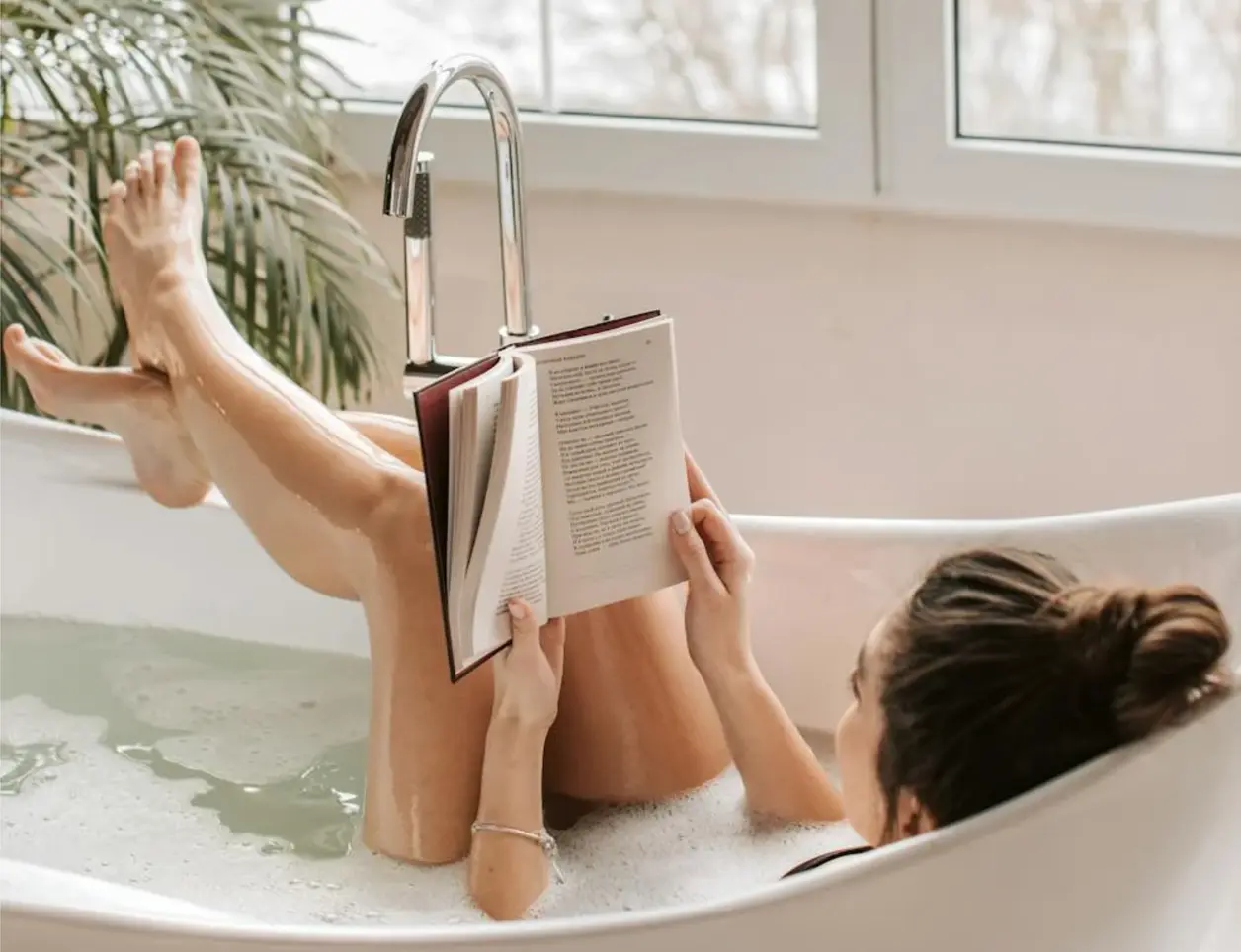 Mujer lee un libro en la bañera con las piernas en alto