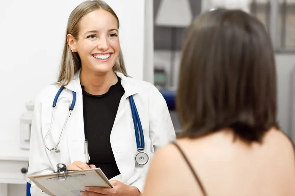 Médica sonriente con estetoscopio toma notas ante una paciente
