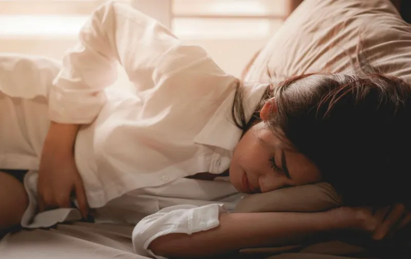 Mujer tumbada de lado en la cama se encoge de dolor con las manos en el vientre