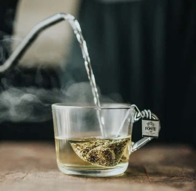 Agua hirviendo vertida en una taza de cristal con una bolsita de infusión