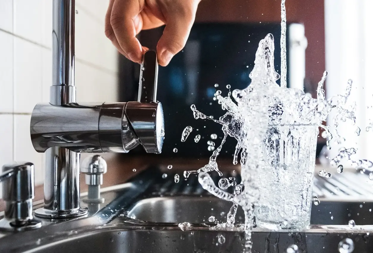 Vaso rebosando bajo el grifo de la cocina con el agua salpicando