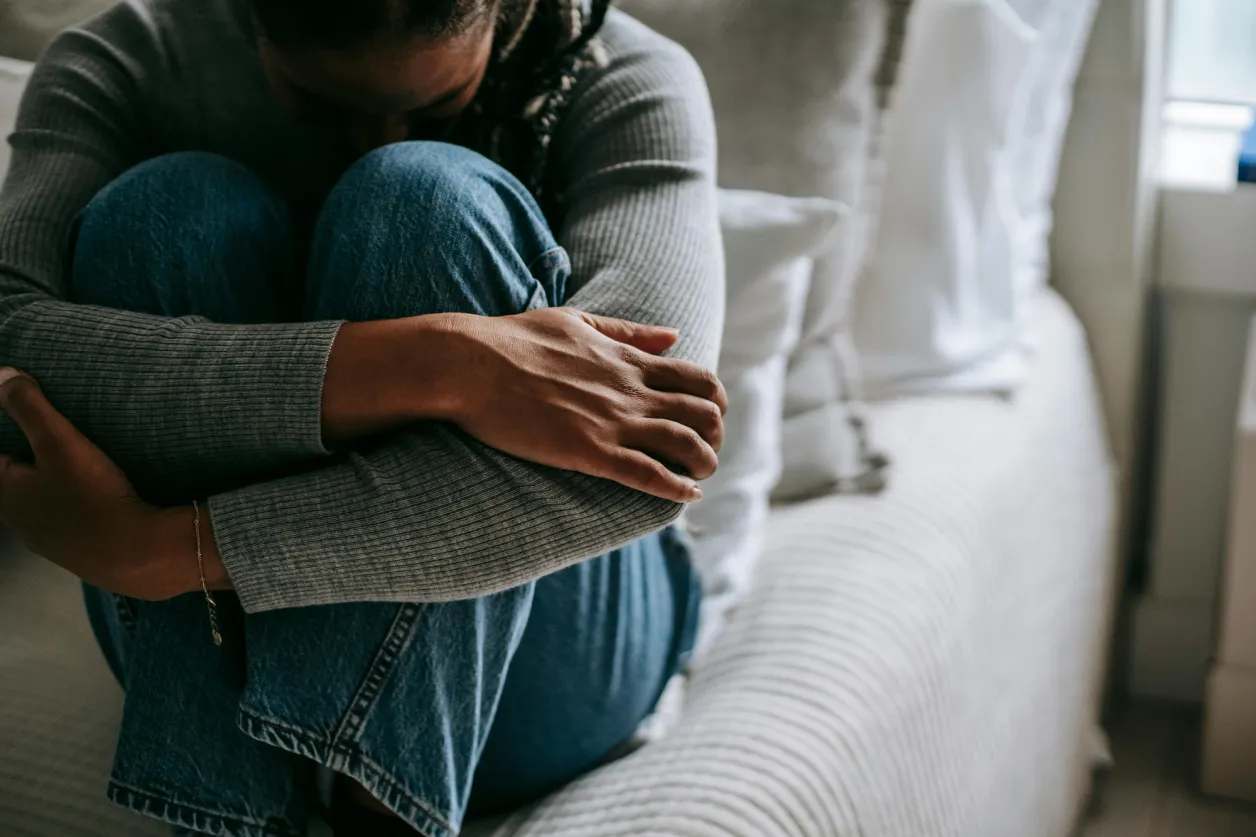 Mujer sentada en un sofá abraza sus rodillas con la cara oculta