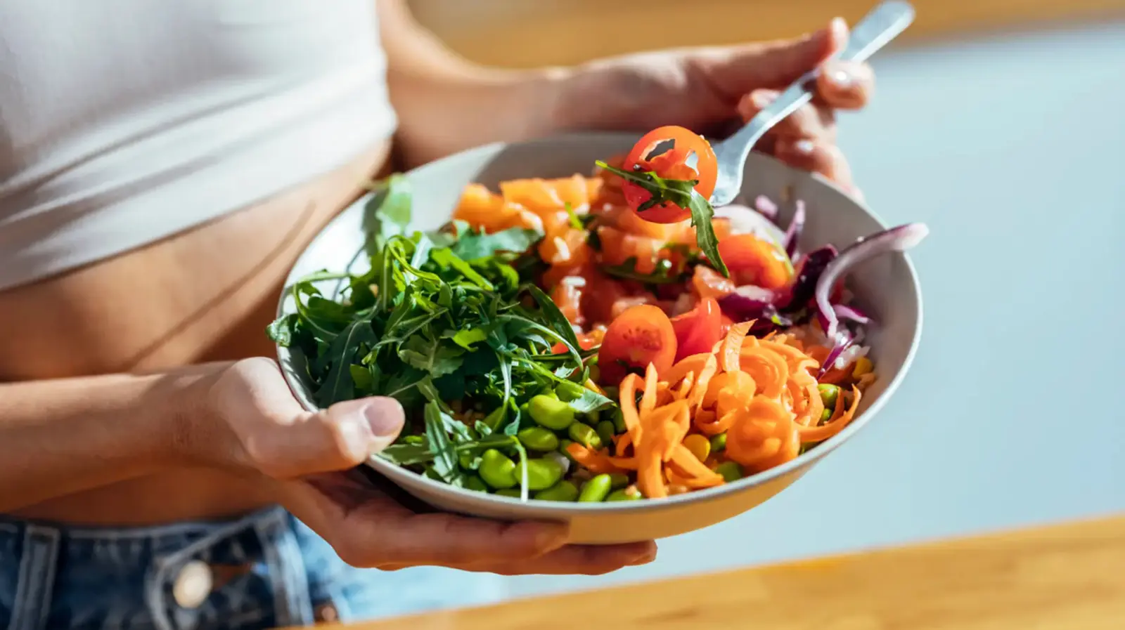 Mujer sostiene un bol de ensalada con salmón, edamame, tomate y zanahoria