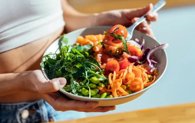 Mujer sostiene un bol de ensalada con salmón, edamame, tomate y zanahoria