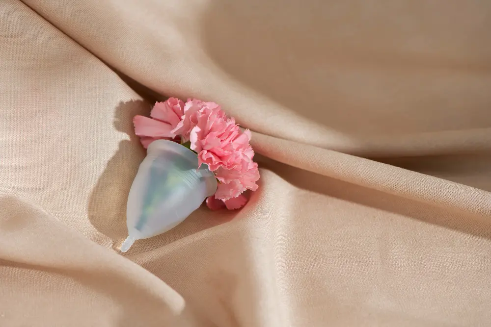 Copa menstrual con una flor rosa sobre una tela beige
