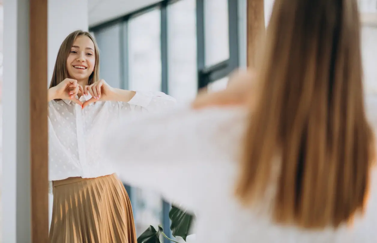 Mujer sonriente forma un corazón con las manos frente al espejo