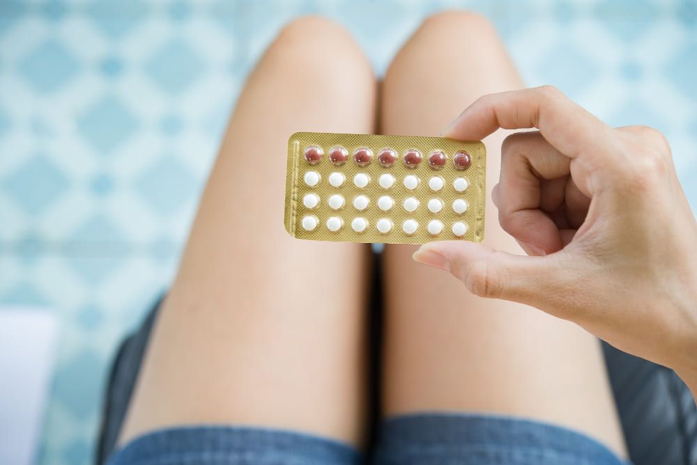 Mano sostiene un blíster de pastillas anticonceptivas sobre las piernas