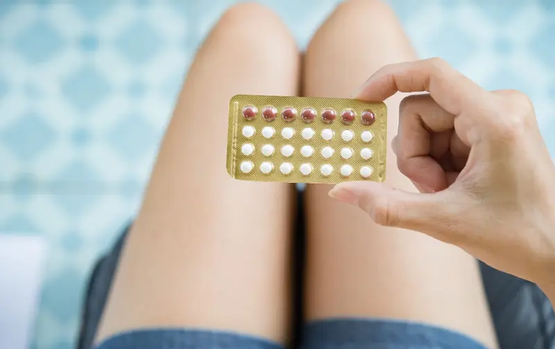 Mano sostiene un blíster de pastillas anticonceptivas sobre las piernas