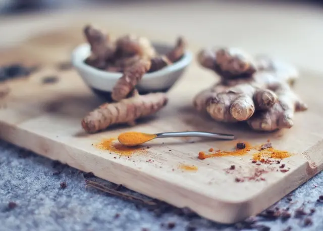 Raíces de jengibre y cúrcuma con cúrcuma en polvo sobre una tabla