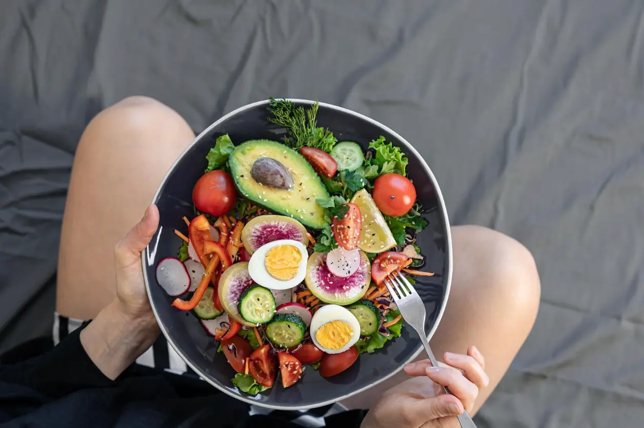 Mujer sostiene un bol de ensalada con huevo, aguacate, tomate y pepino