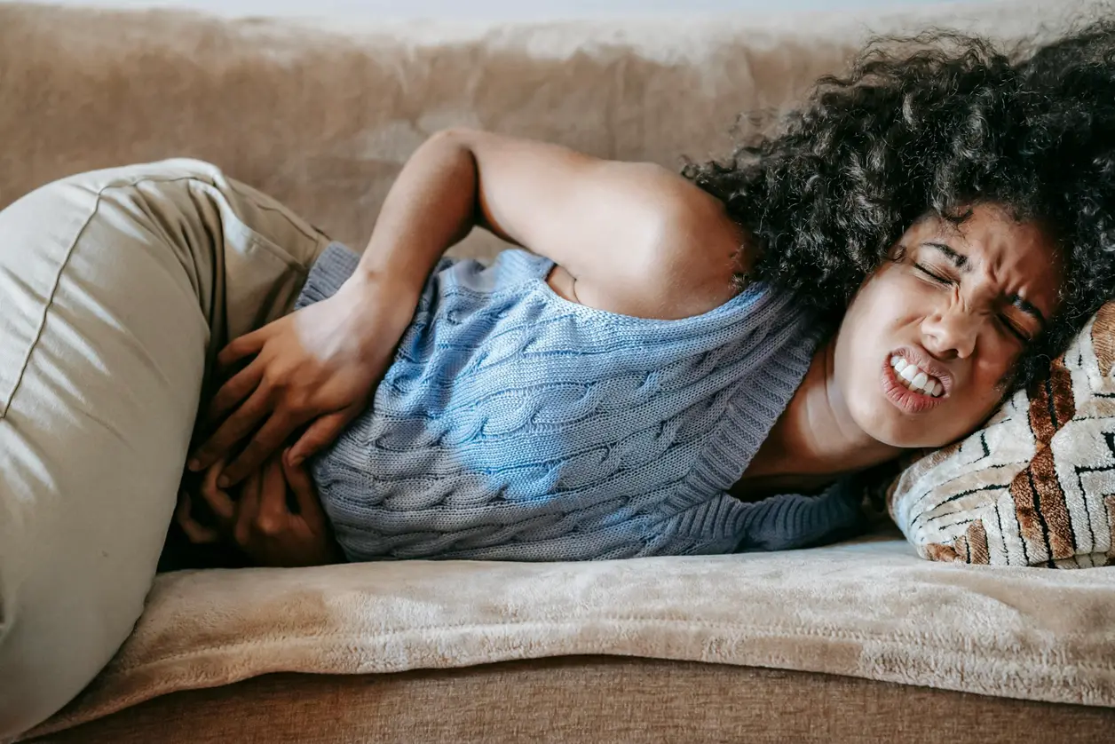 Mujer tumbada en el sofá se encoge de dolor con las manos en el abdomen
