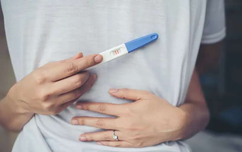 Mujer sostiene un test de embarazo con la otra mano sobre el vientre