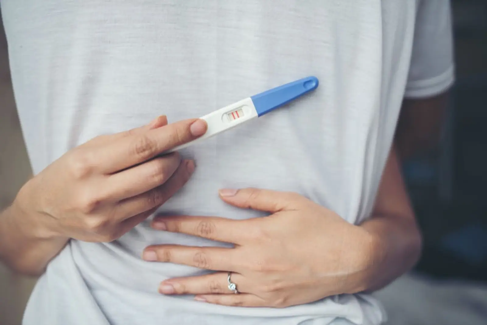 Mujer sostiene un test de embarazo con la otra mano sobre el vientre