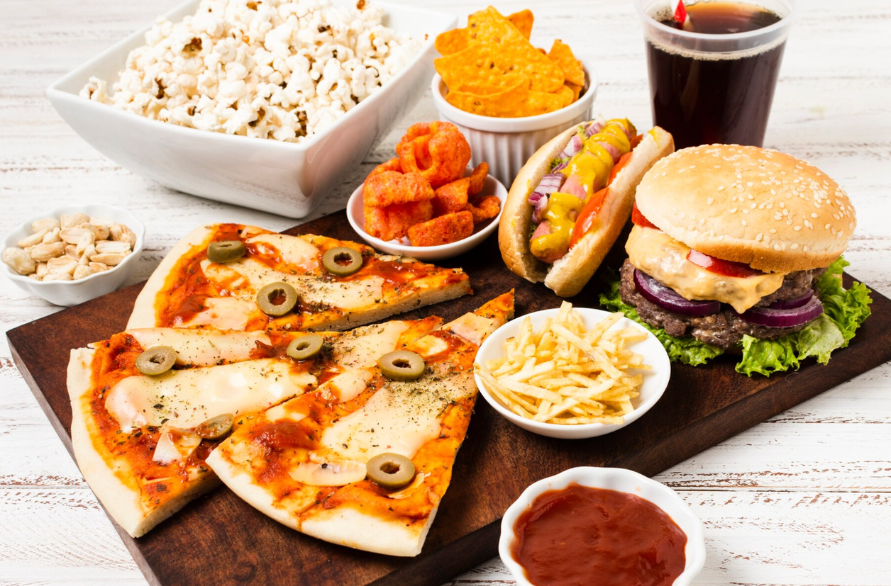 Mesa con pizza, hamburguesa, perrito caliente, patatas fritas, nachos y refresco