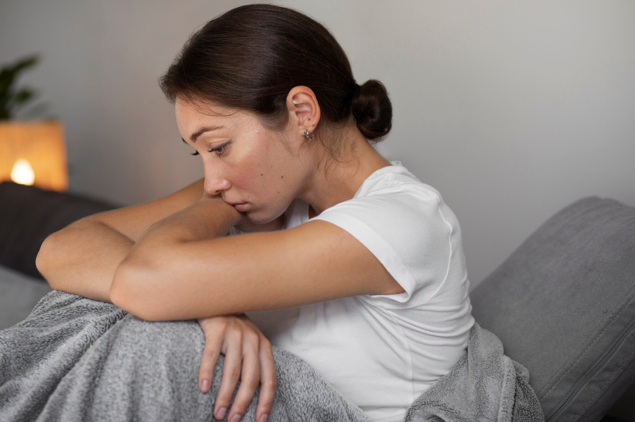 Mujer pensativa abraza sus rodillas sentada en el sofá